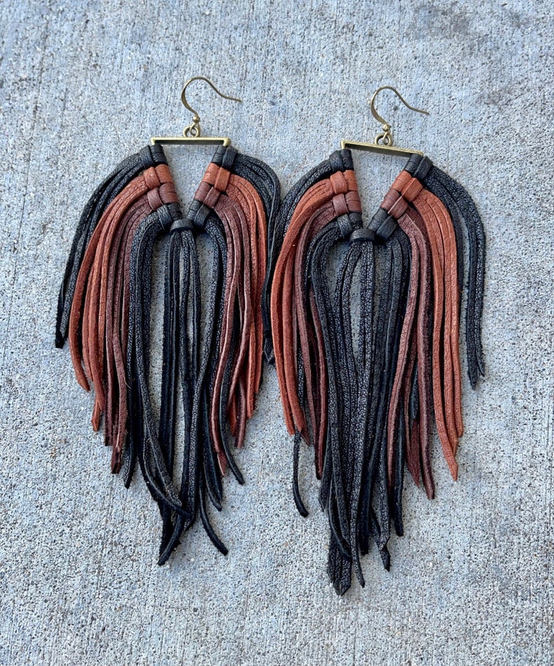 May include: A pair of long, black and brown leather fringe earrings with a triangular metal frame.