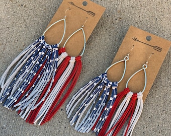 May include: A pair of dangle earrings with red, white, and blue fringe. The fringe is made of leather and has a polka dot pattern. The earrings are on a brown card with an arrow design.