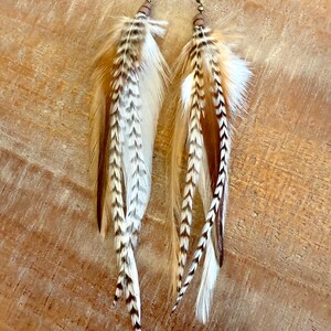 May include: A pair of long feather earrings with brown, white, and black feathers. The earrings are made with a brown bead and a gold hook.