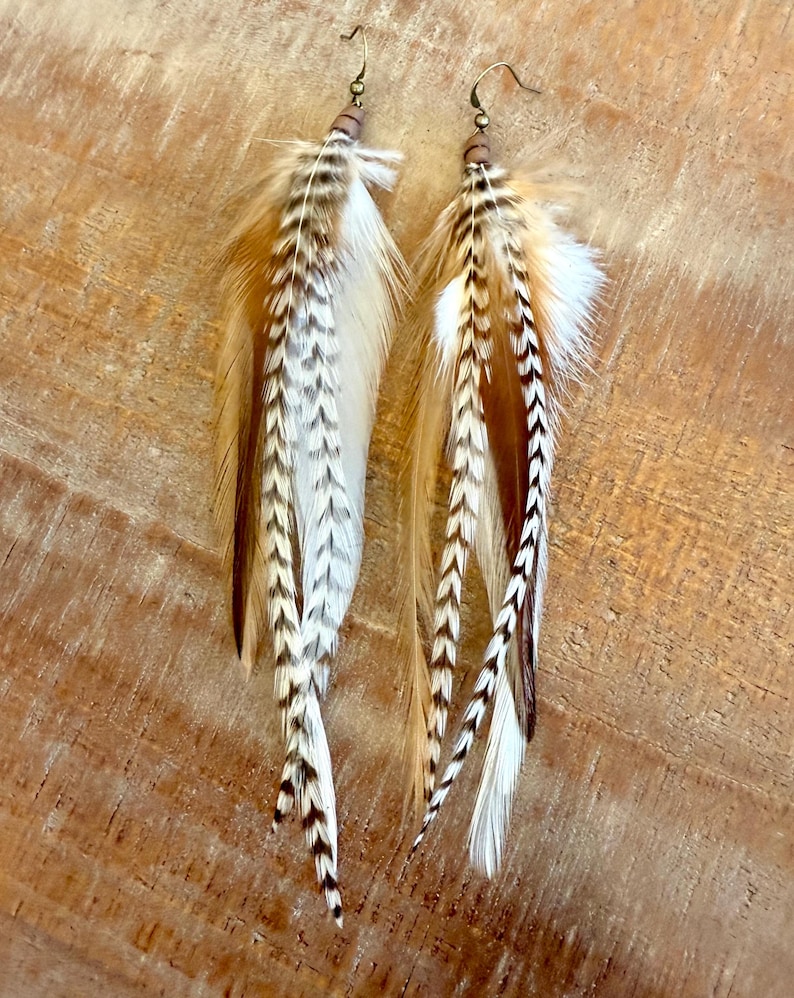 May include: A pair of long feather earrings with brown, white, and black feathers. The earrings are made with a brown bead and a gold hook.