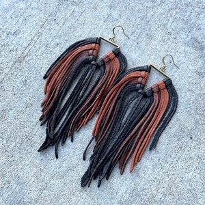 May include: A pair of long, black, brown, and rust colored leather fringe earrings with a square metal frame.