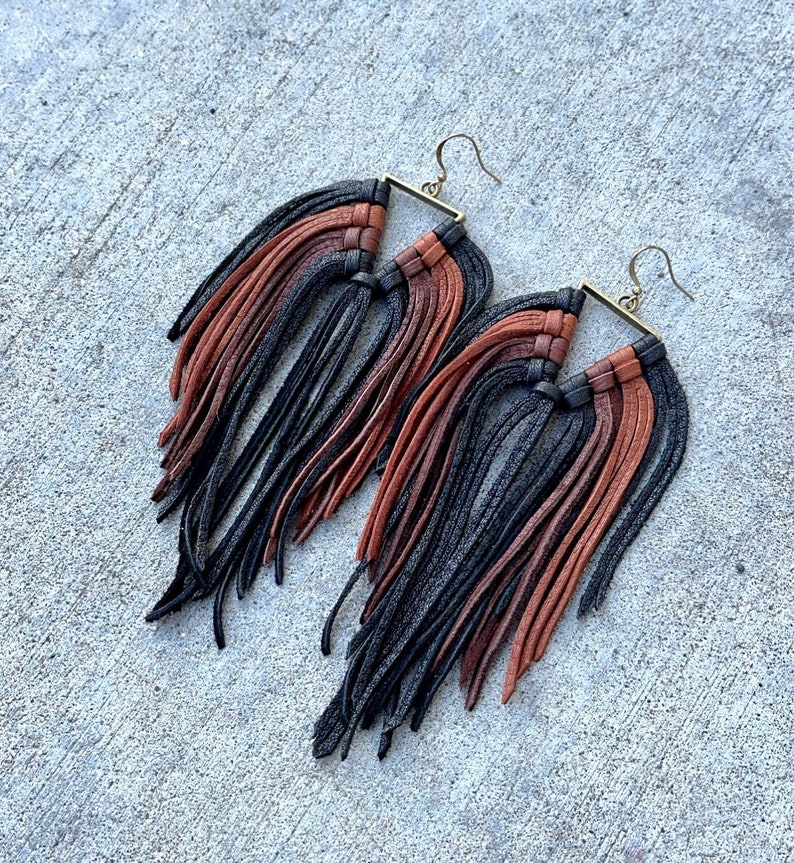 May include: A pair of long, black, brown, and rust colored leather fringe earrings with a square metal frame.