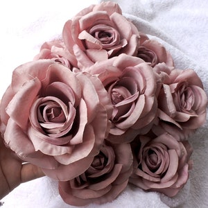 Puede incluir: Un ramo de siete rosas de seda de color rosa polvoriento. Las rosas están dispuestas en un racimo, con los tallos ocultos.