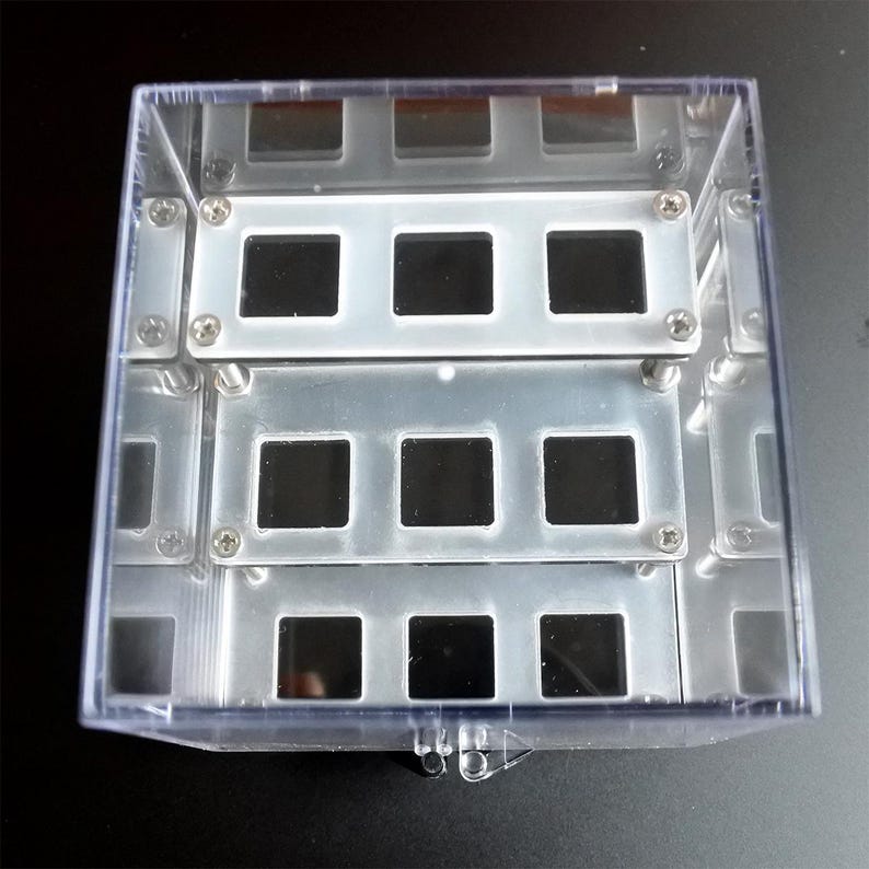 May include: A clear plastic box with a metal insert containing multiple square compartments. The compartments are arranged in three rows of four.