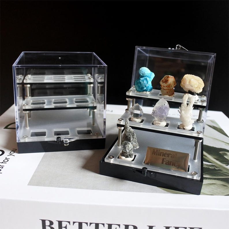 May include: Two clear acrylic display cases for mineral specimens. One case is a cube with three shelves. The other case is a tiered display with three shelves. The tiered display has a label that says "Mineral Fancy".