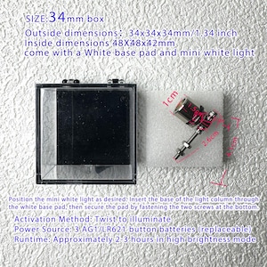 May include: A clear, square display box with a black interior, next to a small, silver and red light fixture on a white pad. The box measures 1.34 inches on each side. The light fixture is 2.6 cm long. Text on the image provides additional details.