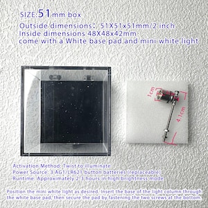 May include: A clear, square display box with a black interior, alongside a white base pad and a small light. The box measures 2 inches on each side. A small light with red and silver accents is also shown.