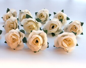 Könnte beinhalten: Ein Dutzend kleine, cremefarbene künstliche Rosen mit grünen Blättern. Die Rosen sind in einer Gruppe auf einer weißen Oberfläche angeordnet.