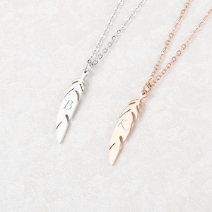 以下が含まれることがあります： 2つの羽根ペンダントネックレス。1つは銀色で、羽根に文字「B」が刻まれています。もう1つはローズゴールド色で、文字「K」が刻まれています。どちらのネックレスも繊細なチェーンが付いています。