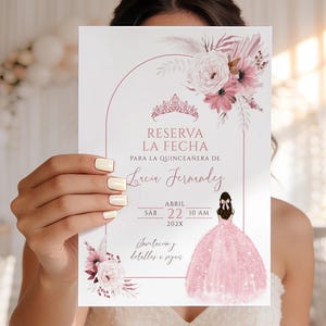 May include: A white invitation card with the text "RESERVA LA FECHA" and "PARA LA QUINCEAÑERA DE" in a pink arch design. The card features floral and crown illustrations, with the date "ABRIL 22 10 AM 202X". The card is held in front of a person wearing a white dress.