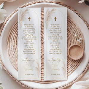 May include: Two baptismal bookmarks with gold cross and text. The text includes a prayer and the date 24 April 202X. The bookmarks are on a white plate with a woven texture, surrounded by flowers and fabric.