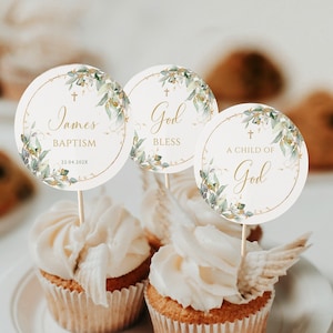 May include: Three white cupcakes with gold and green floral cupcake toppers. The toppers have a cross and the text "James' Baptism 22.04.202X", "God Bless", and "A Child of God".
