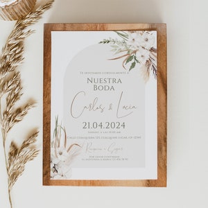 May include: A rectangular wedding invitation card featuring a light gray arch design, white floral illustrations, and brown dried grass accents. The text reads: TE INVITAMOS CORDIALMENTE A NUESTRA BODA Carlos & Lucia 21.04.2024 S&Aacute;BADO, A LAS 10:00 AM.