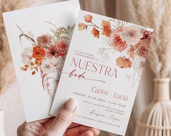 Könnte beinhalten: Zwei weiße Hochzeitseinladungskarten mit floralen Designs in Orange-, Pfirsich- und Burgundertönen. Die Karten enthalten spanischen Text, darunter "Nuestra Boda" und Gästedetails. Die Karten werden von einer Person gehalten.