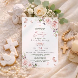 Bautizo invitation flat lay with blush roses, butterflies, cookies, rosary beads, and white roses on lace fabric