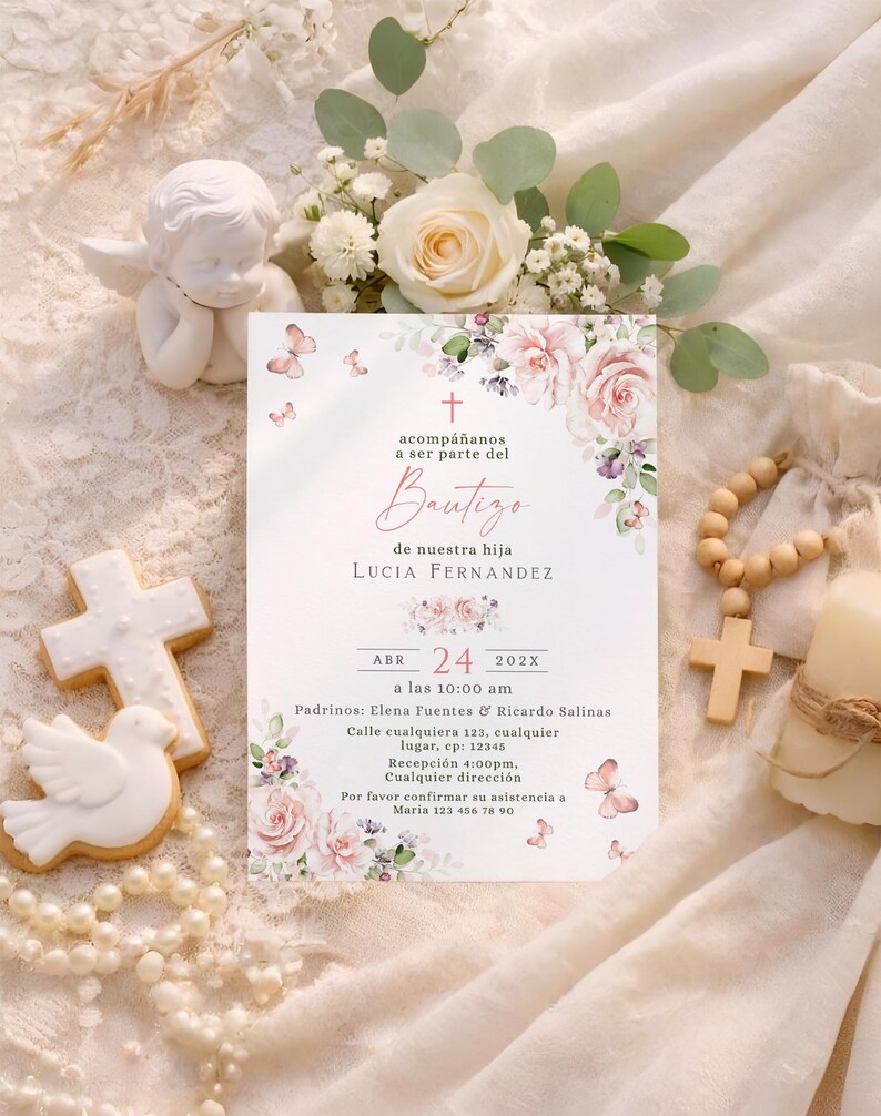 Bautizo invitation flat lay with blush roses, butterflies, cookies, rosary beads, and white roses on lace fabric