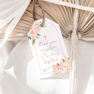 Puede incluir: Una etiqueta blanca de agradecimiento con un diseño floral rosa y una cruz. El texto dice "Gracias por celebrar con nosotros el bautismo de Emilia el 24 de octubre de 202X".