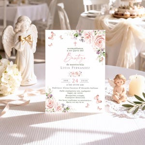 Blush rose butterfly bautizo invitation displayed upright on reception table with angel figurines, candle, and olive branch