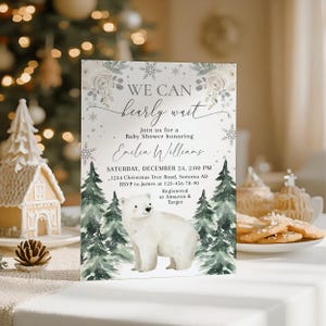 The image is a baby shower invitation featuring a polar bear and a snowy forest scene, with a white background and a festive, wintery theme.