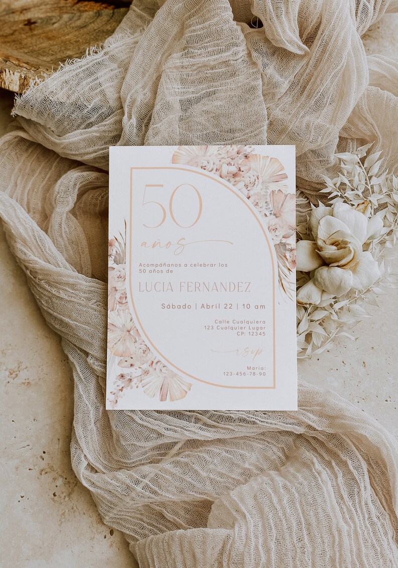 May include: A rectangular invitation card featuring a peach-colored arch graphic, floral illustrations, and the text 50 a&ntilde;os, Acomp&aacute;&ntilde;anos a celebrar los 50 a&ntilde;os de LUCIA FERNANDEZ, S&aacute;bado | Abril 22 | 10 am, Calle Cualquiera 123, and RSVP details.