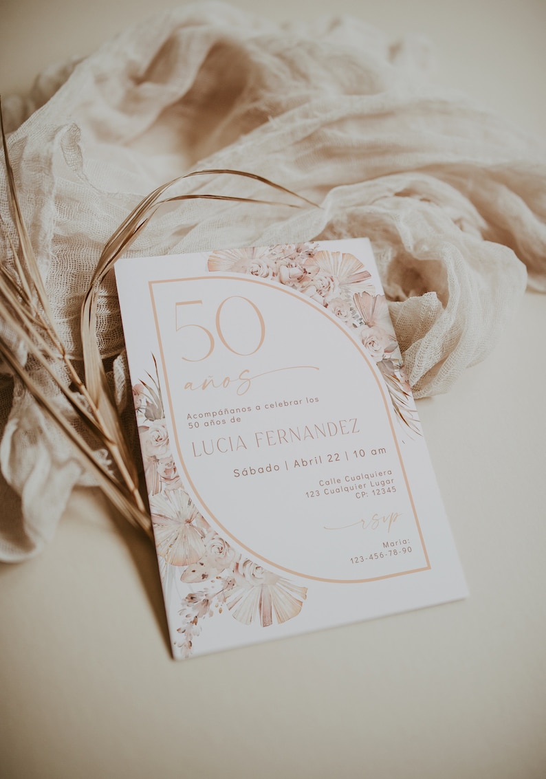 May include: A rectangular invitation card featuring a semi-circular arch design with soft pink and beige floral illustrations. The text reads 50 a&ntilde;os, Acomp&aacute;&ntilde;anos a celebrar los 50 a&ntilde;os de LUCIA FERNANDEZ, S&aacute;bado | Abril 22 | 10 am, and RSVP details.