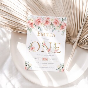 May include: A rectangular birthday invitation card featuring a floral border of pink roses and green leaves at the top and bottom. The text reads EMILIA IS TURNING ONE, PLEASE JOIN US TO CELEBRATE, APRIL 22 AT 10:00AM, 1234 PEACH TREE ROAD, SONOMA AD, RSVP SARAH BY NOVEMBER 22TH AT 123-456-78-90.