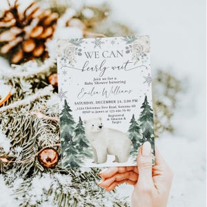 A person is holding a baby shower invitation featuring a polar bear and snowflakes, with a snowy background.