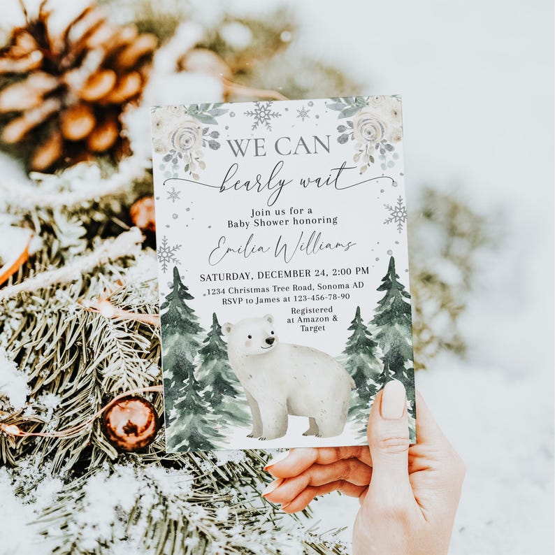A person is holding a baby shower invitation featuring a polar bear and snowflakes, with a snowy background.