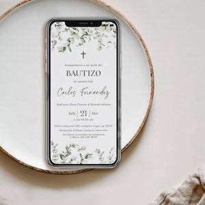 Peut inclure: Un smartphone affiche une invitation de bapt&ecirc;me avec une croix et un motif floral. Le texte de l'invitation comprend le mot "BAUTIZO" et des d&eacute;tails tels que la date, l'heure et le lieu. Le t&eacute;l&eacute;phone repose sur une assiette blanche avec un fond neutre.