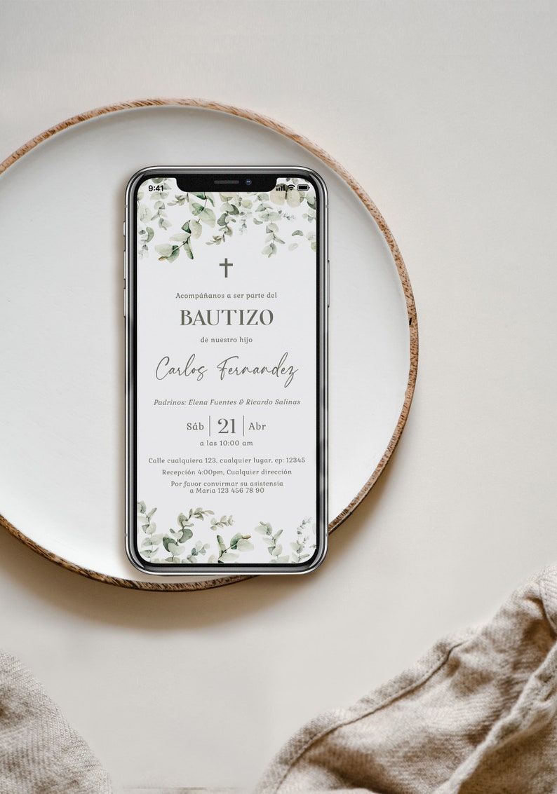 Peut inclure: Un smartphone affiche une invitation de bapt&ecirc;me avec une croix et un motif floral. Le texte de l'invitation comprend le mot "BAUTIZO" et des d&eacute;tails tels que la date, l'heure et le lieu. Le t&eacute;l&eacute;phone repose sur une assiette blanche avec un fond neutre.