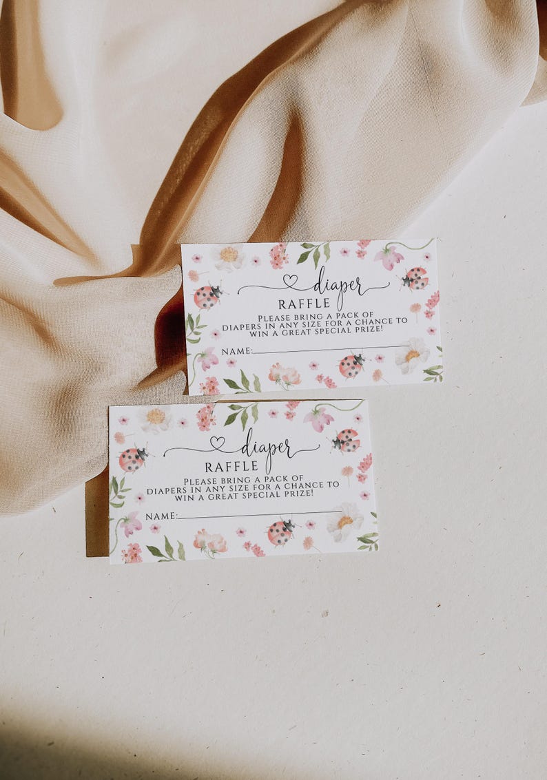May include: Two baby shower raffle tickets with floral and ladybug designs. The tickets read "diaper raffle" and include space for a name. The tickets are decorated with pink flowers and green leaves.
