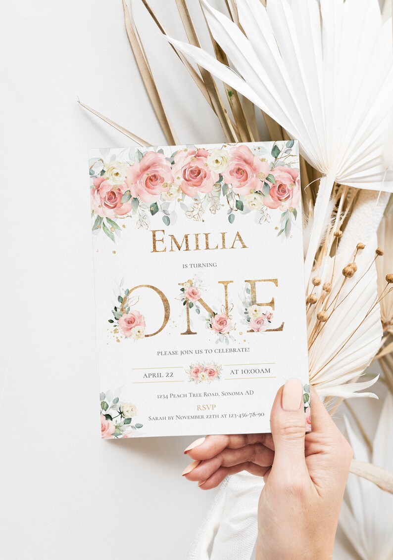 May include: A rectangular invitation card featuring a floral border of pink and white roses with green leaves. The text reads EMILIA IS TURNING ONE, PLEASE JOIN US TO CELEBRATE, APRIL 22 AT 10:00AM, 1234 PEACH TREE ROAD, SONOMA AD, RSVP SARAH BY NOVEMBER 22TH AT 123-456-78-90.