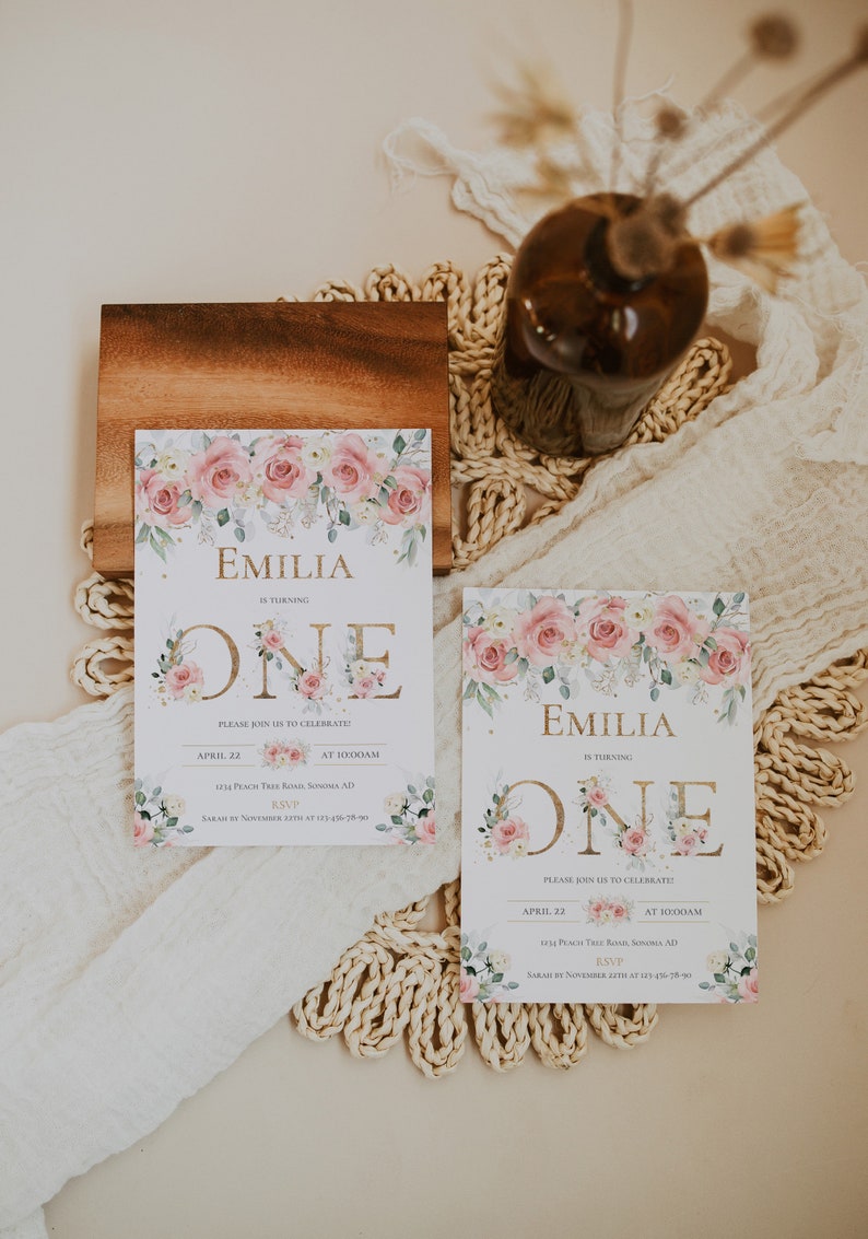 May include: Two rectangular birthday invitation cards featuring a watercolor floral border of pink roses and green leaves. The text reads Emilia is turning one, with event details including the date April 22, time 10:00AM, and location 1234 Peach Tree Road.
