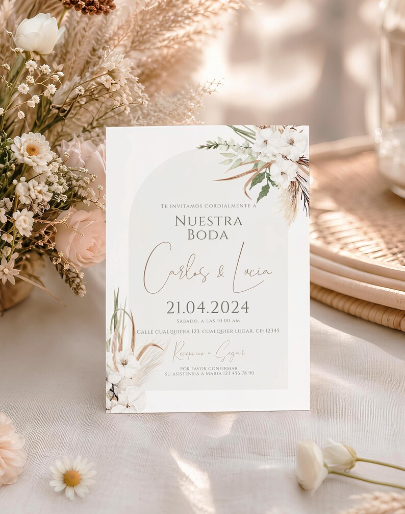 May include: A rectangular wedding invitation card featuring a soft sage green arch graphic, white floral illustrations, and dried pampas grass accents. The text reads: TE INVITAMOS CORDIALMENTE A NUESTRA BODA, Carlos & Lucia, 21.04.2024, SABADO, A LAS 10:00 AM, CALLE CUALQUIERA 123, CUALQUIER LUGAR, CP: 12345, Recepcion a Seguir, POR FAVOR CONFIRMAR SU ASISTENSIA A MARIA 123 456 78 90.