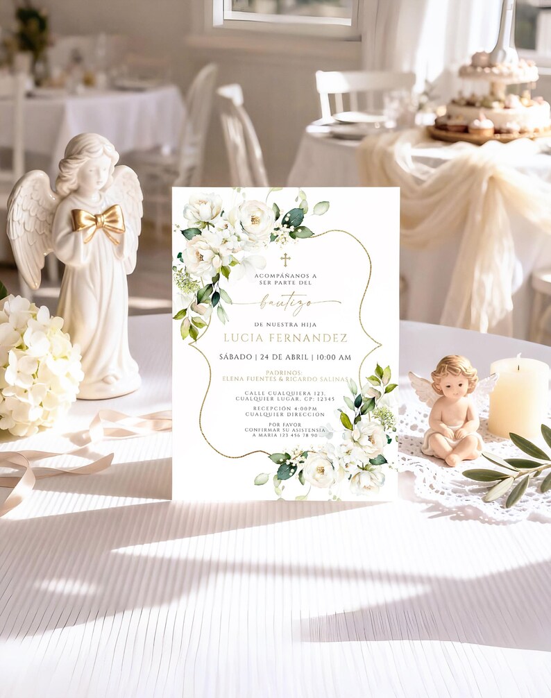 White floral bautizo invitation displayed upright on reception table with angel figurines, candle, and olive branch
