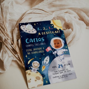 Könnte beinhalten: Eine blaue und gelbe Weltraum-Geburtstagseinladung für einen Jungen namens Carlos, der drei Jahre alt wird. Die Einladung zeigt einen Cartoon-Astronauten, der eine Flagge hält, ein Raumschiff, einen Bären im Raumanzug und ein UFO. Der Text lautet "3... 2... 1... A DESPEGAR! Carlos Cumple Tres Años ESTAS. INVITADO A MI CUMPLEAÑOS!" Die Einladung enthält auch das Datum, die Uhrzeit und den Ort der Party.
