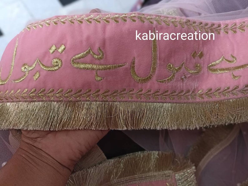May include: Pink fabric with gold embroidery of Arabic script. The fabric has a gold fringe trim. The text reads "kabiracreation".