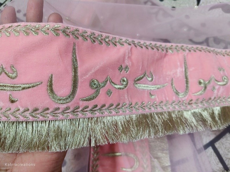 May include: Pink velvet fabric with gold embroidery of Arabic script. The fabric has a gold fringe trim.