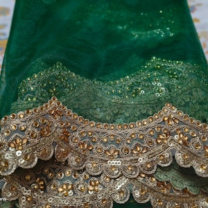 Op de afbeelding: Close-up van een groene stof met ingewikkelde gouden borduursels en pailletten. De stof heeft een gelaagd ontwerp, met een geschulpte rand. De algehele esthetiek is elegant en geschikt voor speciale gelegenheden.
