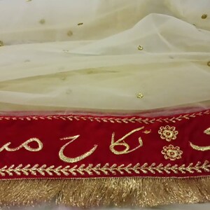 May include: A white sheer fabric with gold sequins and a red velvet trim with gold embroidery that reads "Ladi ki Maa"