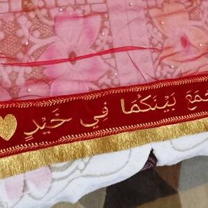 May include: Red fabric with gold trim and a red velvet ribbon with gold embroidery and Arabic text. The text reads "Ma sha Allah wa la quwwata illa billah" and "I love you" in Arabic.