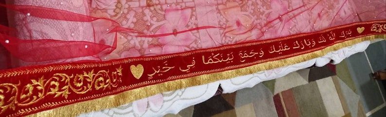 May include: Red fabric with gold trim and a red velvet ribbon with gold embroidery and Arabic text. The text reads "Ma sha Allah wa la quwwata illa billah" and "I love you" in Arabic.