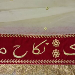 May include: A red velvet banner with gold embroidery featuring the words "Bari Ka Sajda" in Arabic script. The banner has a gold fringe trim and is decorated with small gold flowers.