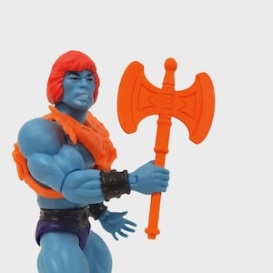 Pode incluir: Uma figura de ação azul com cabelo ruivo e um machado laranja. A figura está vestindo uma armadura laranja, um tapa-sexo roxo e botas roxas. A figura está segurando o machado na mão direita.