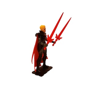 Può includere: Statuetta di un personaggio con capelli biondi corti, che indossa un abito nero e grigio con un mantello rosso. Il personaggio tiene in mano due grandi spade rosse. La statuetta è su una base nera.