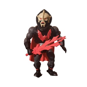 May include: A vintage action figure of a character in black and grey armour with a red cape and a red weapon. The figure has a pale face with black facial features and a black helmet. The figure is standing on a white background.