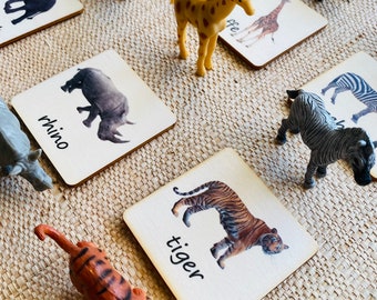 May include: A set of wooden flash cards featuring different animals, including a lion, giraffe, rhino, tiger, zebra, and elephant. Each card has a picture of the animal and the animal's name written below it.