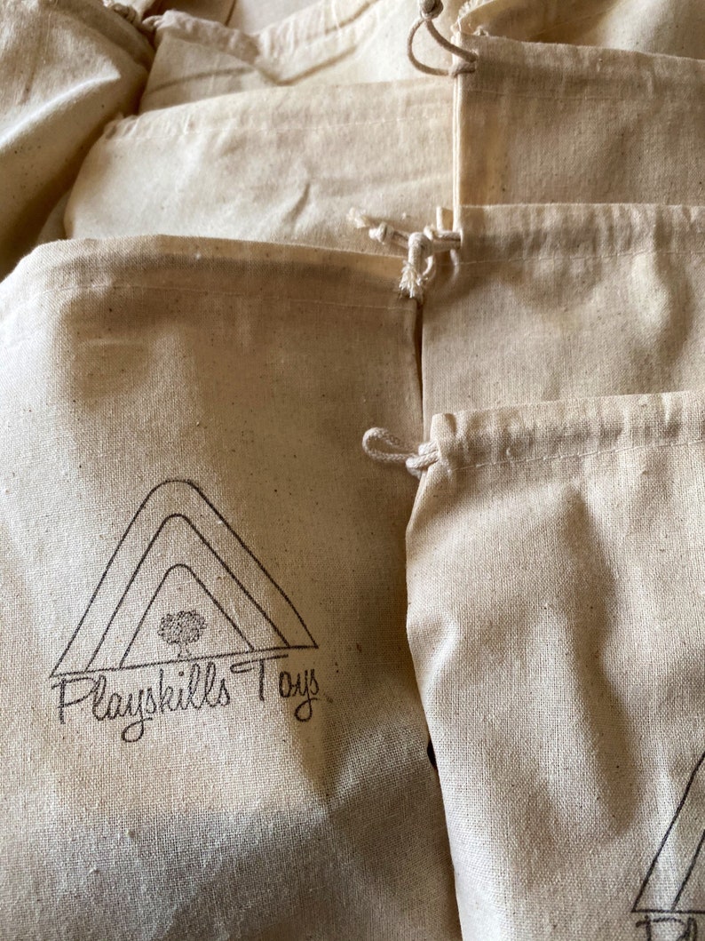 May include: A stack of natural cotton muslin drawstring bags with a logo that reads "Playskills Toys" printed on the front of one of the bags.
