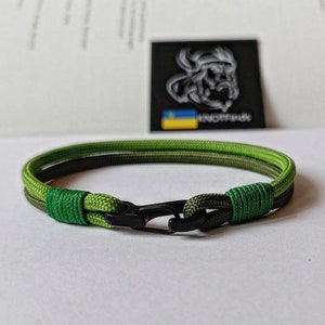 May include: A green and dark green paracord bracelet with a black metal clasp.