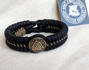 Op de afbeelding: Zwart paracord armband met een goudkleurige metalen bedel met het Vegvisir-symbool, een Noors directioneel symbool. Het armband is gevlochten met een tan paracord.